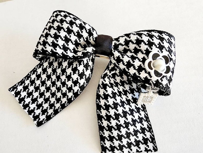May include: A black and white houndstooth bow with a silver flower accent and a dangling crystal charm.