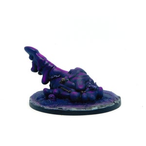 May include: A purple and pink miniature figurine of a blob-like creature with bones and skulls on a black base.