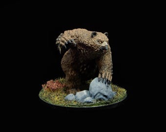 Pode incluir: Figura em miniatura detalhada de um urso pardo em pose ameaçadora, em pé sobre uma base gramada com rochas e folhagem. O urso tem uma expressão ameaçadora e está sobre um fundo preto.