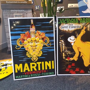 K&ouml;nnte beinhalten: Zwei Vintage-Emaille-Schilder. Das linke Schild ist eine Martini-Werbung mit einer gr&uuml;nen, gelben und wei&szlig;en Trauben-Traube mit einem Gesicht. Das rechte Schild ist eine Victoria Arduino-Kaffeew Werbung mit einem Mann in einem gelben Anzug, der Kaffee gie&szlig;t.