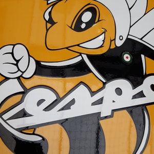 K&ouml;nnte beinhalten: Ein gelbes und schwarzes Vespa-Scooter-Logo mit einer Cartoon-Biene, die einen Helm tr&auml;gt. Die Biene h&auml;lt eine Faust und das Wort "Vespa" ist in wei&szlig;en Buchstaben auf dem Roller geschrieben.