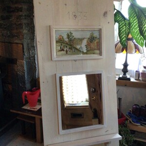 Puede incluir: Un espejo de madera blanco con un estante, una peque&ntilde;a imagen enmarcada de una cascada y el n&uacute;mero 1833 tallado en la madera.