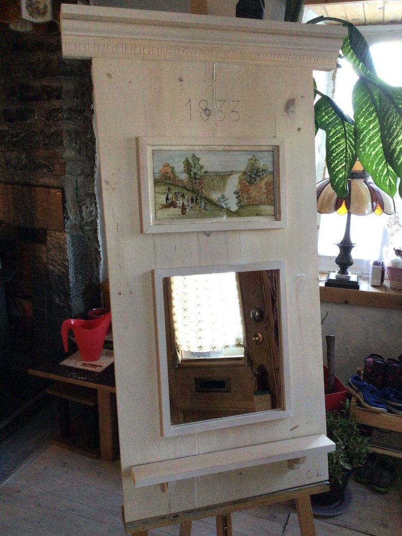 Puede incluir: Un espejo de madera blanco con un estante, una peque&ntilde;a imagen enmarcada de una cascada y el n&uacute;mero 1833 tallado en la madera.