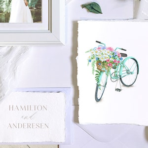 Puede incluir: Una bicicleta azul claro con una cesta de mimbre llena de flores de colores. La bicicleta tiene neum&aacute;ticos blancos y un manillar blanco. Las flores son rosas, moradas, blancas y azules.