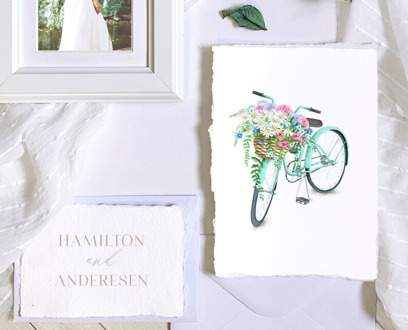 Puede incluir: Una bicicleta azul claro con una cesta de mimbre llena de flores de colores. La bicicleta tiene neum&aacute;ticos blancos y un manillar blanco. Las flores son rosas, moradas, blancas y azules.