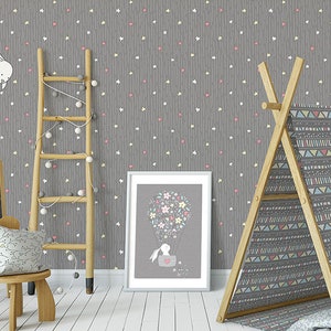 K&ouml;nnte beinhalten: Eine graue Kinderzimmertapete mit einem wei&szlig;en und rosa Sternenmuster. Die Tapete zeigt ein sich wiederholendes Muster aus Sternen und Herzen. Eine Holzleiter, ein Tipi-Zelt und ein gerahmtes Bild sind im Hintergrund.