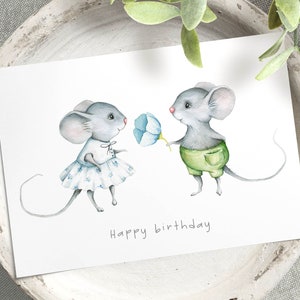 May include: A watercolor illustration of two mice, one in a blue dress and the other in green shorts, holding a blue flower. The text "Happy birthday" is written below the mice.