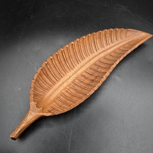 May include: A wooden leaf-shaped tray, carved with intricate detail. The tray is made from light brown wood, featuring a textured surface and veining. This decorative leaf design is suitable for serving or display, measuring approximately 40 cm in length.