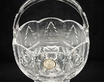 May include: A clear 24% lead crystal basket with a scalloped rim and a fixed arched handle. The exterior features etched pine tree motifs and geometric diamond cuts. A circular gold sticker on the front reads Made in Poland 24% Lead Crystal.
