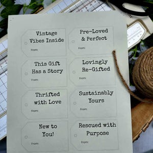 Puede incluir: Una hoja de etiquetas de regalo imprimibles con frases como «Vintage Vibes Inside» y «Pre-Loved & Perfect». Las etiquetas verde claro tienen texto negro. Tijeras y cuerda en el fondo. Las etiquetas están diseñadas para regalar.