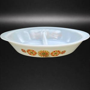 May include: Oval, divided serving dish in white with a floral pattern in orange, yellow, and green. The dish has a handle in the center, and is likely made of glass or ceramic.