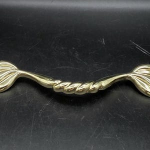 Peut inclure: Une poignée de meuble dorée avec un motif de queue de sirène à chaque extrémité et un centre torsadé en forme de corde. La quincaillerie est en métal et est conçue pour les meubles.