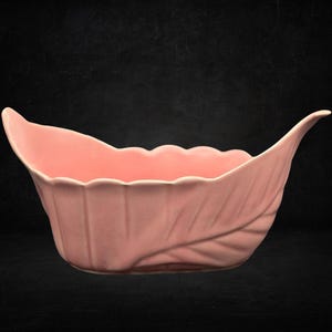 May include: A matte pink ceramic bowl shaped like a stylised leaf with a scalloped rim and a pointed, upturned end. The exterior features embossed vein details that mimic the natural structure of a leaf, creating a textured surface.