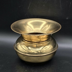 May include: A vintage brass vessel with a wide, flared top and a rounded base. The brass has a warm, golden hue and a slightly aged appearance. The vessel is likely used for decorative or functional purposes.