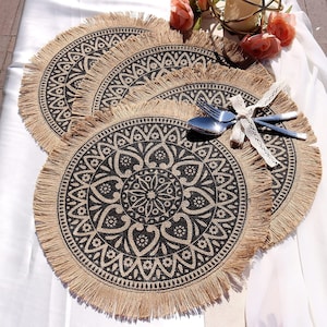 May include: Set of three round jute placemats with a black and cream mandala design and fringe trim.