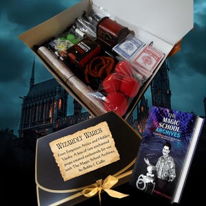 Puede incluir: Una caja abierta llena de accesorios de magia, incluyendo naipes, bolas de esponja roja, un pequeño cofre de madera y una baraja de cartas. También se ve un libro titulado "The Magic School Archives", junto con un sobre negro con el texto "Wizardly Wares".