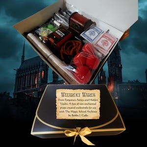 Può includere: Una scatola aperta piena di oggetti di scena, tra cui carte da gioco, un piccolo forziere in legno, palline rosse e una corda. La scatola è etichettata "Wizardly Wares" e contiene il testo "Multiplying Rabbits". La scatola è decorata con un fiocco dorato.