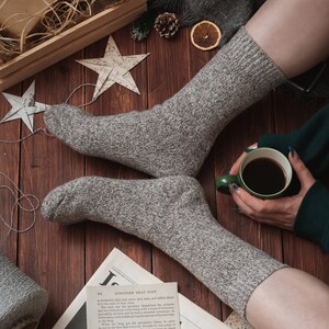 May include: A pair of grey knitted socks with a cup of coffee and a newspaper on a wooden surface. The newspaper has the headline "STRONGER THAN FATE".