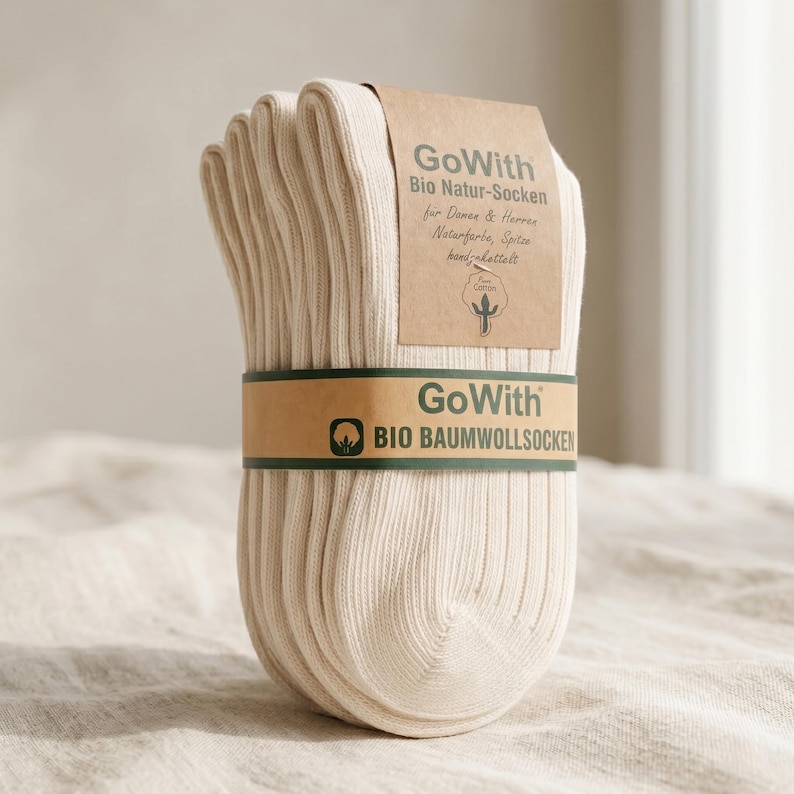 K&ouml;nnte beinhalten: Ein B&uuml;ndel cremefarbener gerippter Socken, zusammengehalten von einem braunen Band. Das Band und ein Etikett zeigen den Text "GoWith" und "Bio Natur-Socken". Die Socken sind aus Bio-Baumwolle.