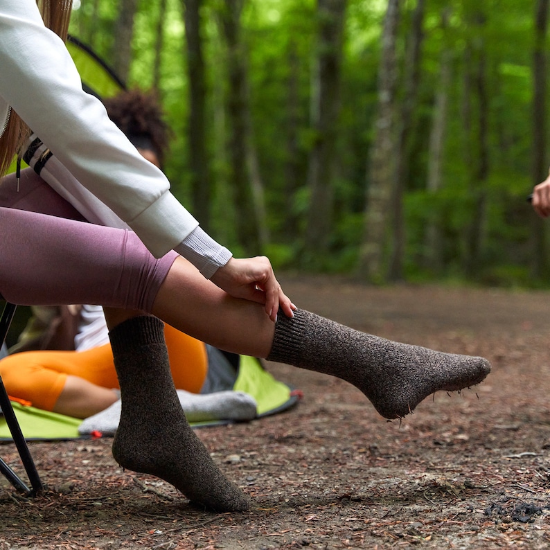 May include: A woman wearing brown socks sits on a green camping chair in a woodland setting. The socks are made of a soft, textured material and have a comfortable fit.