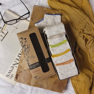 May include: A box of GoWith Linen socks with a gray and white pattern and colorful trim. The box is brown and has the text "The Ultimate Socks" and "GoWith Linen" on it. The socks are designed for people with diabetes.