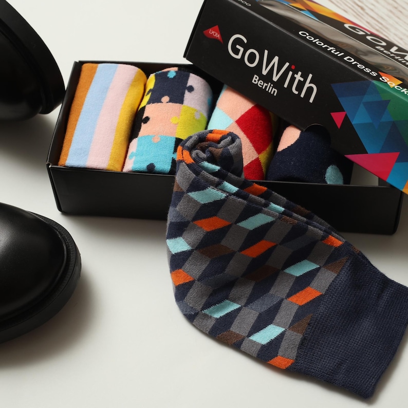 May include: A black box set of colorful dress socks with the text "Go With Berlin." The socks feature various patterns, including stripes, polka dots, and geometric designs. A pair of black shoes is visible in the background.