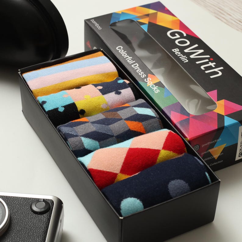 May include: A black box containing six pairs of colorful dress socks. The socks have various patterns, including stripes, polka dots, and geometric designs. The box has the text "Go With Berlin" and "Colorful Dress Socks."