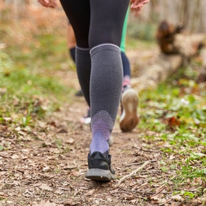 May include: Close-up of a person's legs wearing black leggings and a pair of grey and purple compression socks. The person is walking on a path in a forest.