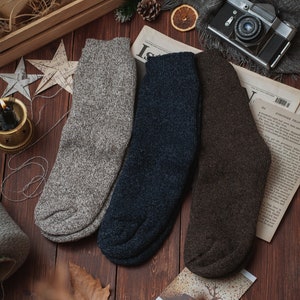 May include: Three pairs of wool socks in grey, navy blue, and brown. The socks are folded and arranged on a wooden surface.