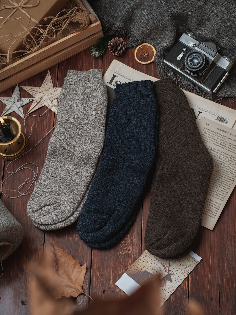 May include: Three pairs of wool socks in grey, navy blue, and brown. The socks are folded and arranged on a wooden surface.