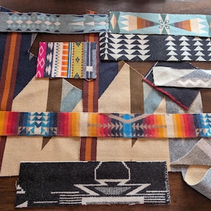 May include: Assortment of fabric swatches with geometric patterns in various colors. The swatches include designs with triangles, diamonds, and stripes. Colors include blue, orange, red, and beige. The fabrics appear to be woven.