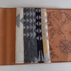May include: A brown leather journal with a compass and map design on the cover. The journal has a flap that opens to reveal a patterned fabric lining.