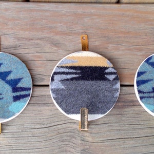 May include: Three round wall hooks with a geometric pattern in shades of blue, gray, and yellow. Each hook is made of metal and has a brass finish.