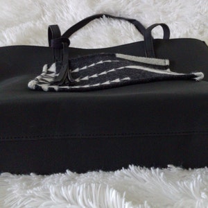 May include: Black tote bag with a black and white patterned fabric lining. The bag has two handles and a zipper closure.
