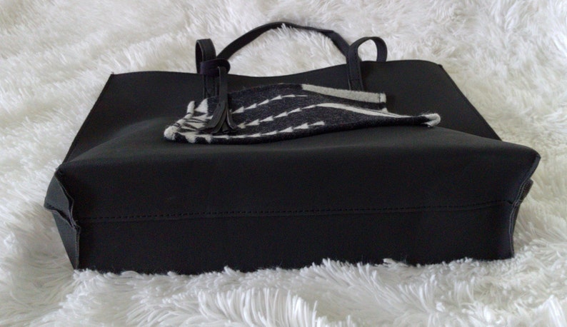 May include: Black tote bag with a black and white patterned fabric lining. The bag has two handles and a zipper closure.