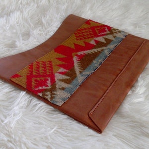 May include: A brown leather clutch with a colorful geometric patterned fabric insert. The fabric is red, yellow, blue, and brown.