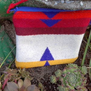 May include: A small, colorful zippered pouch made of woven fabric. The pouch has a white background with red, yellow, and blue geometric patterns.