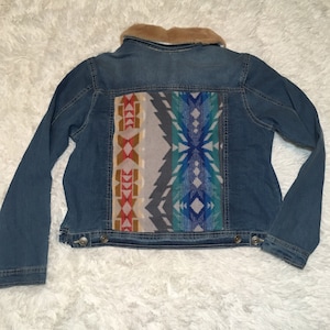 May include: A blue denim jacket with a faux fur collar and a colorful geometric patterned fabric panel on the back.