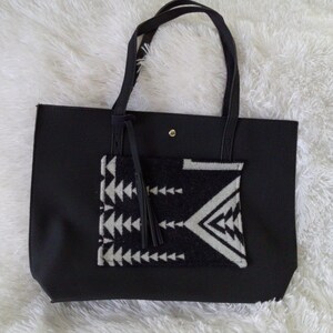 May include: Black tote bag with a geometric patterned pocket and a tassel. The bag has a black strap and a gold button.