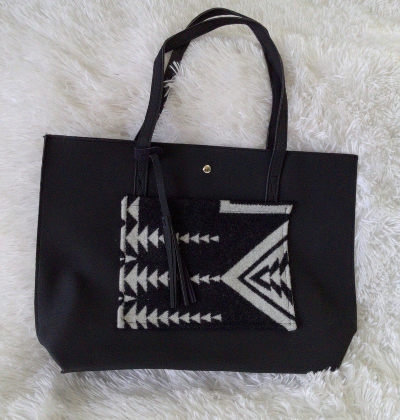 May include: Black tote bag with a geometric patterned pocket and a tassel. The bag has a black strap and a gold button.