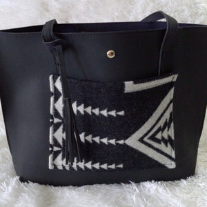 May include: Black leather tote bag with a black and white geometric patterned pocket and a black tassel.
