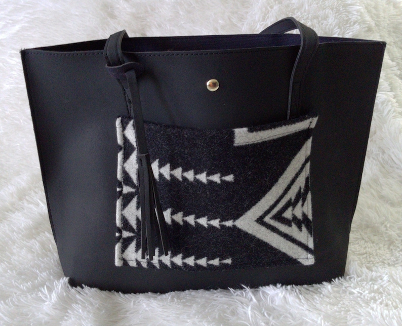 May include: Black leather tote bag with a black and white geometric patterned pocket and a black tassel.