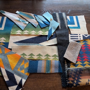 May include: Assortment of fabric swatches with geometric patterns in various colors, including blue, green, yellow, and red. The swatches are arranged on a dark wooden surface, showcasing a variety of designs and textures.