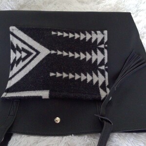 May include: Black leather tote bag with a black and white geometric patterned fabric pocket and a black tassel.