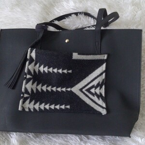 May include: Black tote bag with a black and white geometric patterned pocket on the front. The bag has two black straps and a black tassel.
