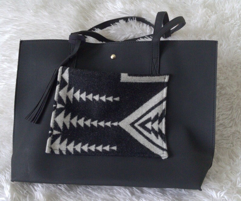 May include: Black tote bag with a black and white geometric patterned pocket on the front. The bag has two black straps and a black tassel.