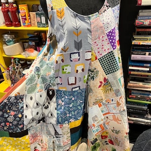 Puede incluir: Un vestido sin mangas de patchwork con una variedad de patrones coloridos, incluyendo estampados florales, geométricos y de animales. El vestido está hecho de diferentes telas y tiene una silueta suelta y fluida.