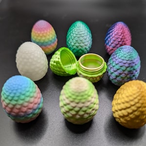 May include: A collection of nine colorful dragon egg-shaped trinket boxes. The boxes are made of a textured plastic and come in a variety of colors, including green, blue, pink, yellow, and white. Some of the boxes are open, revealing a small, empty interior.