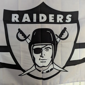 May include: Black and white flag with the word "RAIDERS" in a large, bold font. The flag features a stylized pirate skull with an eyepatch and crossed swords.