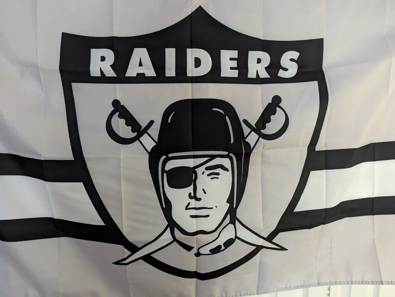 May include: Black and white flag with the word "RAIDERS" in a large, bold font. The flag features a stylized pirate skull with an eyepatch and crossed swords.